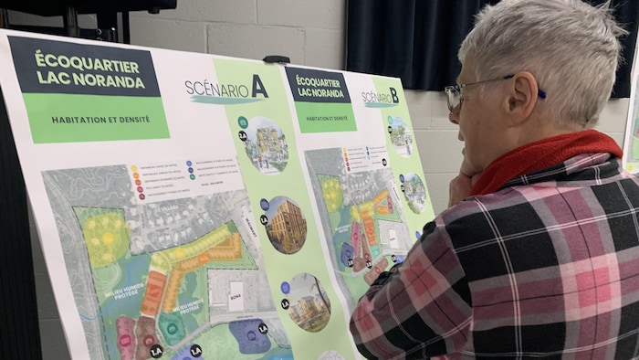 Une femme regarde les détails du scénario A et du scénario B pour l'écoquartier du lac Noranda.
