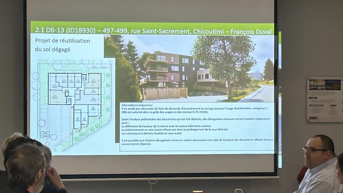 Une présentation concernant la démolition d'un bâtiment de la rue Saint-Sacrement, à Chicoutimi, est projetée sur un mur. 