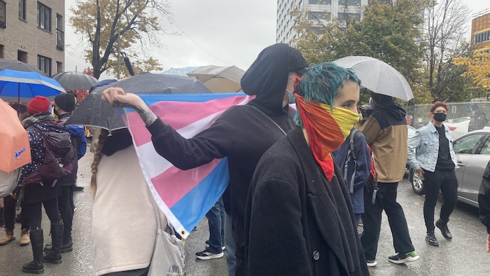 Contre-manifestants avec des drapeaux LGBTQ+, sous la pluie.
