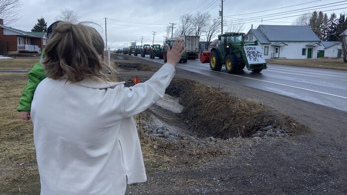 Une dame salue un convoi de tracteurs qui passe devant sa résidence.
