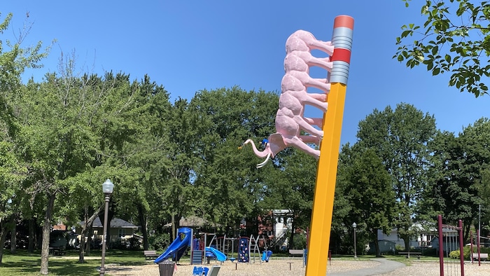 Un éléphant-chenille descend sur un crayon de bois géant, dans un parc. 
