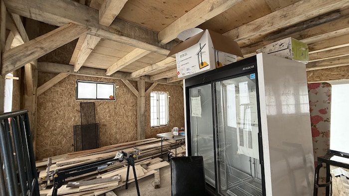 L'intérieur d'un édifice en construction où l'on voit des outils de menuiserie, un réfrigérateur commercial et la charpente en bois massif.