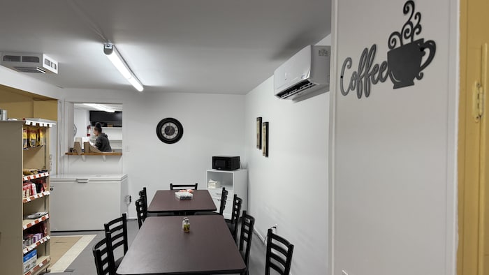 Une salle avec deux tables et des chaises. Sur le mur, on voit la affiche qui dit Coffee avec un café fumant.