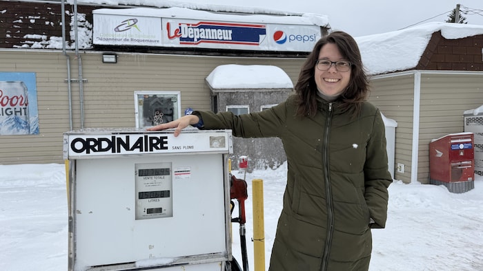 Karine Péladeau est debout, une main sur une pompe à essence ordinaire qui montre son âge devant le dépanneur de Roquemaure.