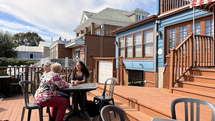 Des membres de la coopérative profitant d'une terrasse ensoleillée à Tadoussac, discutant de l'avenir de leur projet.