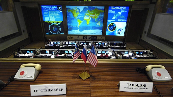 Un bureau avec deux téléphones, des petits drapeaux, avec un écran géant à l'avant. 