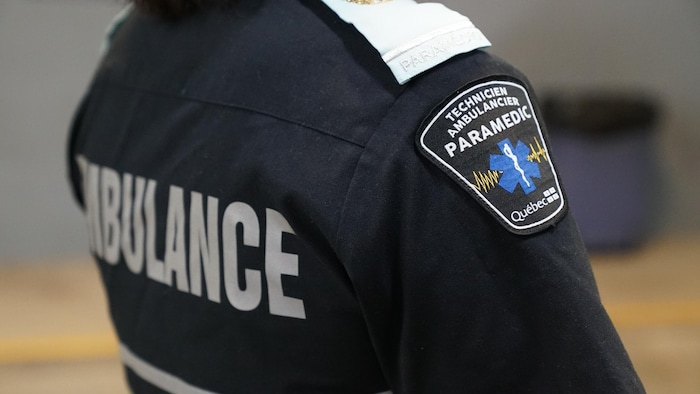 Une femme porte une chemise sur laquelle se trouve un écusson portant l'inscription « Technicien ambulancier - Paramédic - Québec ».