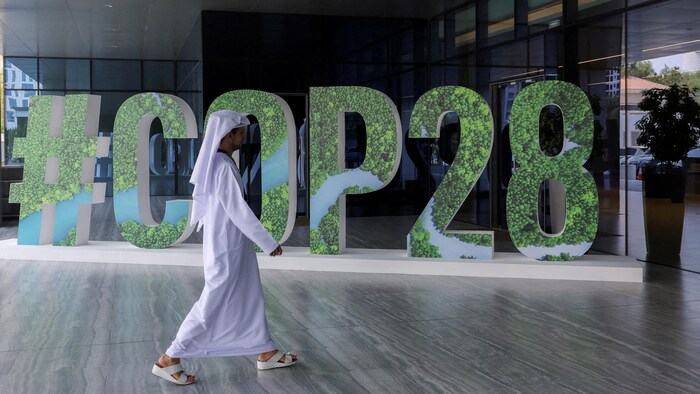  Une personne passe devant un grand panneau #COP28.