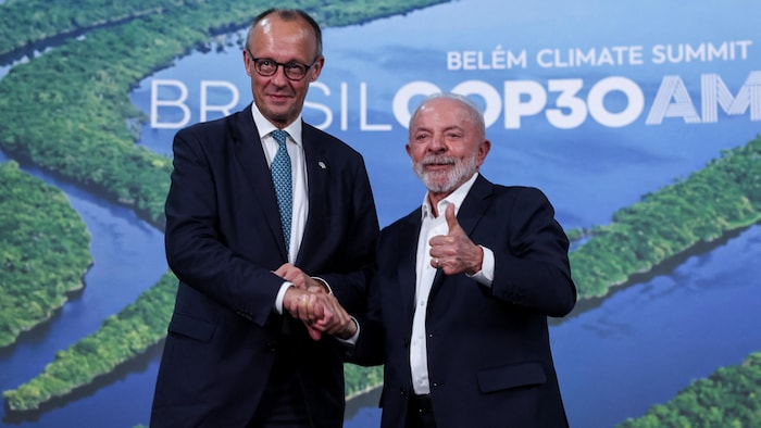 Le président brésilien Luiz Inacio Lula da Silva et le chancelier allemand Friedrich Merz se serrent la main devant le logo de la COP30.