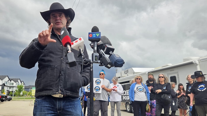 Le chanteur Corb Lund debout devant des partisans lors d'une conférence de presse