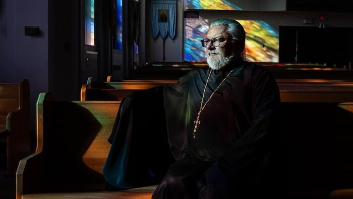 Cornell Zubritsky en robe de prêtre orthodoxe noire est assis sur un des bancs de la cathédrale orthodoxe ukrainienne Saint-Jean-Baptiste.