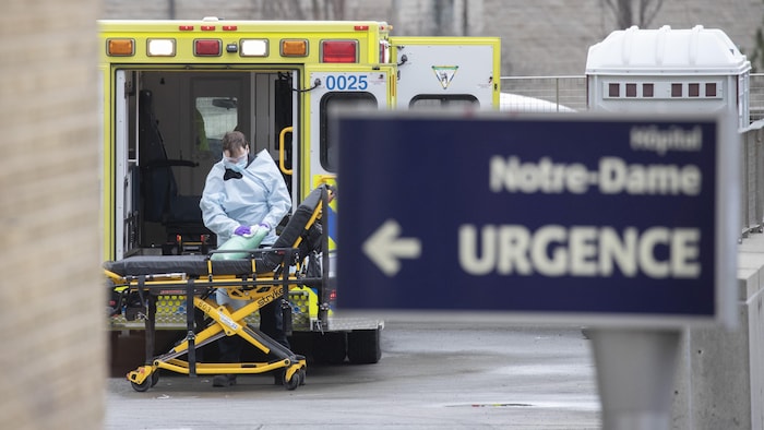 Un homme en habit de protection nettoie un coussin près d'une ambulance à l'urgence de l’hôpital Notre-Dame, à Montréal.