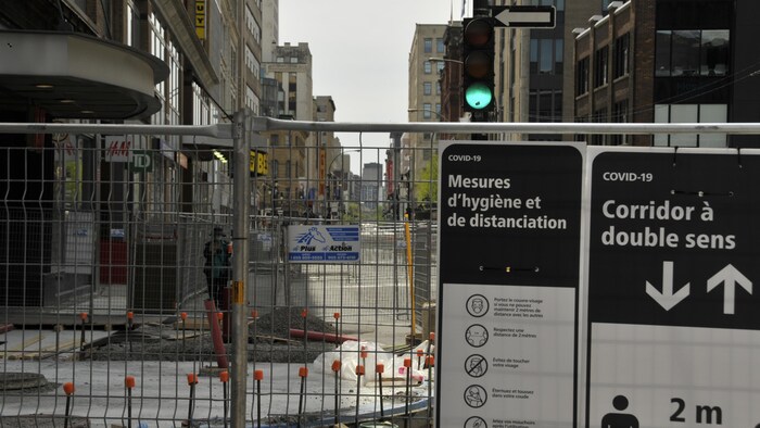 Des clôtures dans le centre-ville de Montréal avec des panneaux indiquant les mesures d'hygiène et de distanciation sociale à respecter.