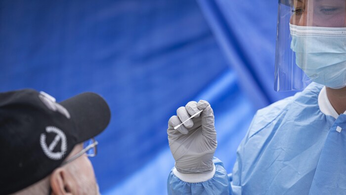 Un homme s'apprête à subir un test de dépistage de la COVID-19 par une professionnelle de la santé.