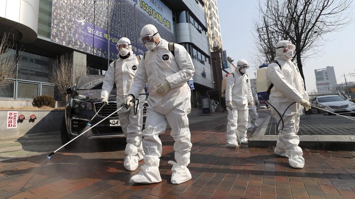 Des ouvriers en combinaison et masques désinfectant les rues de Daegu