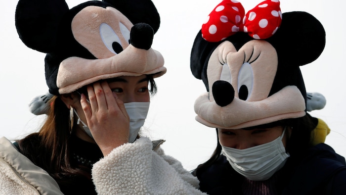 Deux femmes portant des casques de Mickey et Minnie portent des masques.