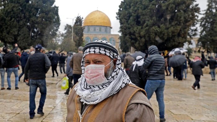Un Palestinien porte un masque. Le dôme du Rocher se profile derrière lui. 