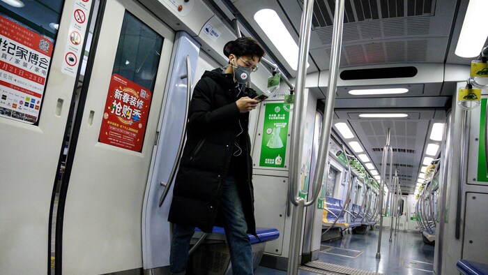 Une homme porte un masque pour se protéger du coronavirus en consultant son téléphone dans un wagon de métro vide, à Pékin. 