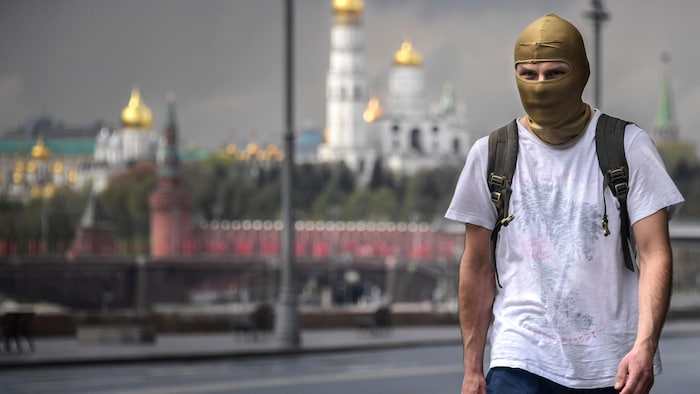 Un homme portant une cagoule dorée marche. Derrière lui, on voit le Kremlin.