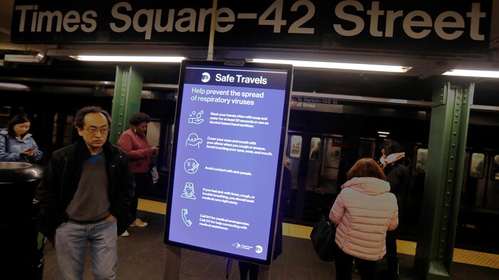 Des passagers du métro passent près d'une affiche indiquant quoi faire pour éviter de contracter la maladie.