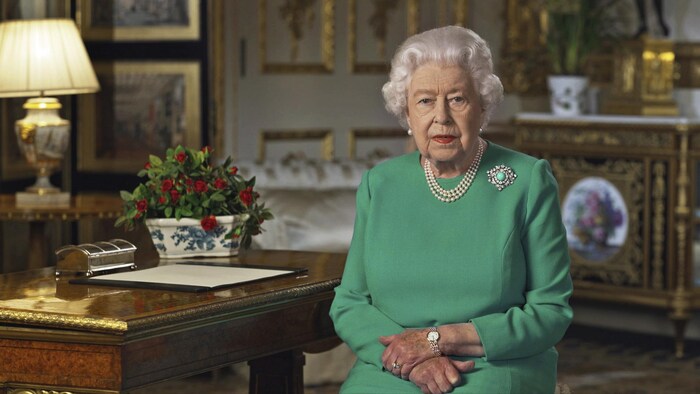 La reine Élisabeth II assise à un bureau dans une salle du château de Windsor.