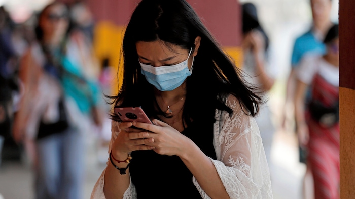 Une femme regarde son téléphone. Elle porte un masque facial pour se protéger du coronavirus. 