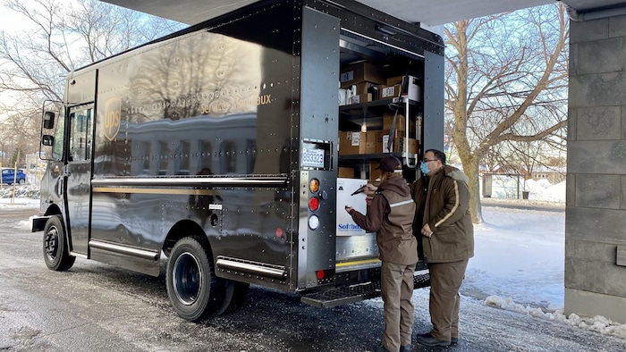 Des employés d'UPS scannent une boîte à l'arrière de leur camion. 