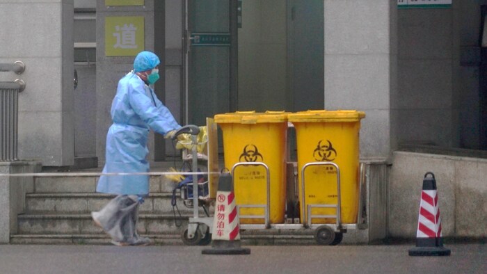 Un homme en vêtements de protection transporte des contenants de déchets biomédicaux.