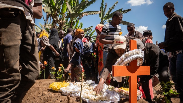 Des gens pleurent autour d'une tombe fraîchement creusée.