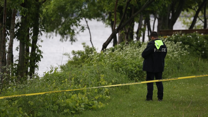 Un policier devant un cours d'eau. Une scène policière est érigée.