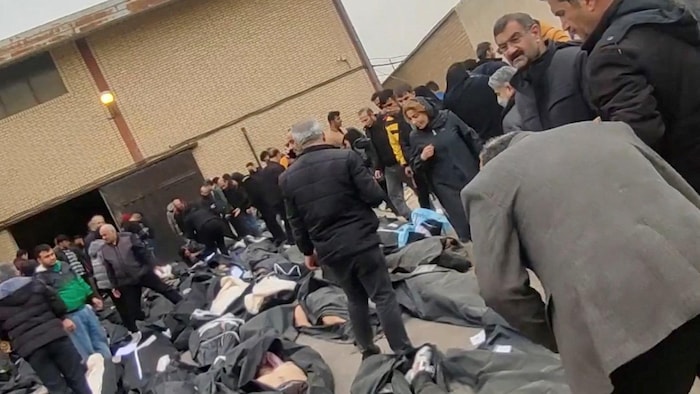 Des personnes circulent entre des cadavres dans des housses noires qui jonchent le sol.