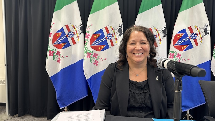 Cory Bellmore sourie au micro devant des drapeaux du Yukon.