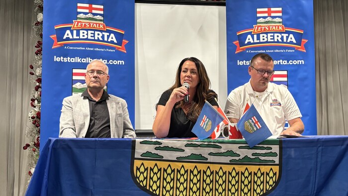 Une femme et deux hommes assis à une table avec des drapeaux albertains.