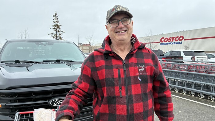 Un homme qui porte un manteau, un chapeau et des lunettes devant un Costco. 