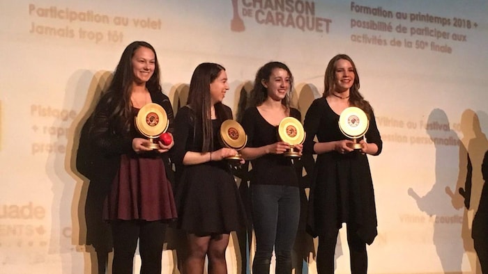 Quatre jeunes artistes tiennent leur trophée en main sur une scène.