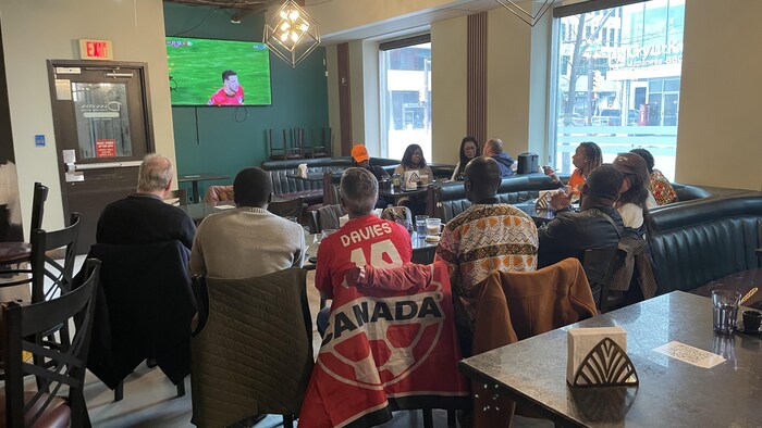 Une douzaine de personnes regardent la télé.