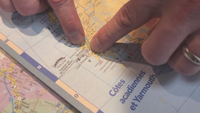 Des doigts pointent Yarmouth et la région touristique des Côtes acadiennes sur une carte étalée sur une table.