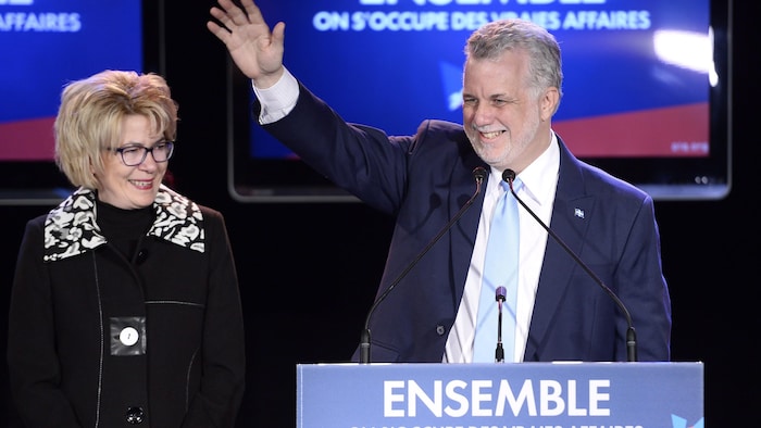 Philippe Couillard lève la main   en souriant.