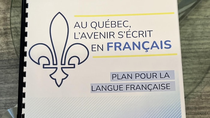 Sur une table, un document officiel du gouvernement du Québec où il est inscrit « Au Québec, l'avenir s'écrit en français : Plan pour la langue française ».