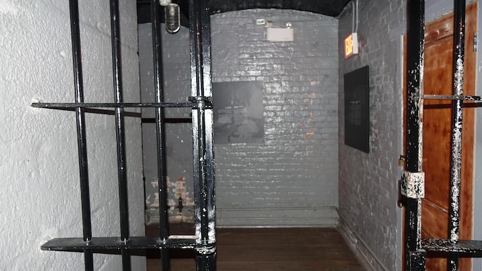 Une porte à barreaux de fer derrière laquelle on voit un mur de pierre blanc.