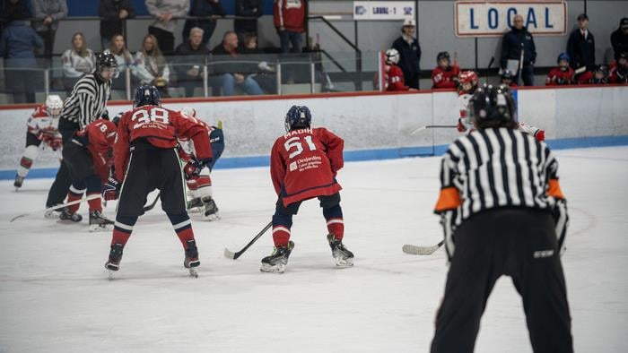 Des jeunes joueurs de hockey en action sur la glace sous l'oeil d'un arbitre.
