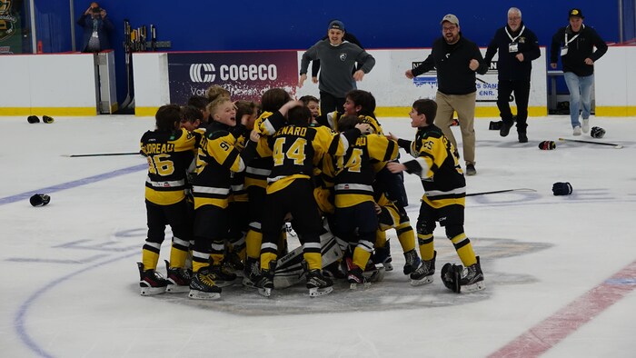 L'équipe gagnante de la coupe célèbre la victoire sur la patinoire, rejointe par les entraîneurs.