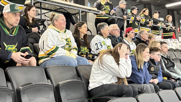 Une jeune femme aux cheveux longs assise dans les gradins de l'aréna se saisit la tête à deux mains, courbe l'échine et apparaît catastrophée par ce qui se passe dans le match.