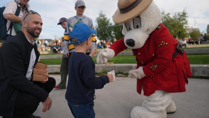 Un enfant tendant la main pour recevoir une branche d'une mascotte de la GRC.