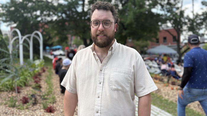 Un homme dans un parc, derrière un rassemblement de personnes assises.