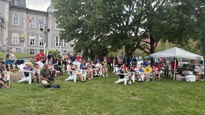 Une soixantaine de personnes sont dans un parc et regarde vers un écran qui diffuse un match de soccer.