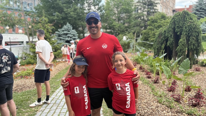Ils sont tous trois dans un espace urbain, portant le chandail de l'équipe nationale de soccer du Canada.