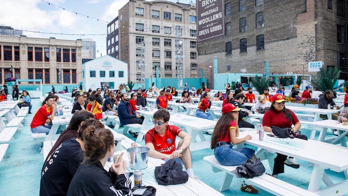Des amateurs de soccer assis à de nombreuses tables à pique-nique sur une vaste terrasse.