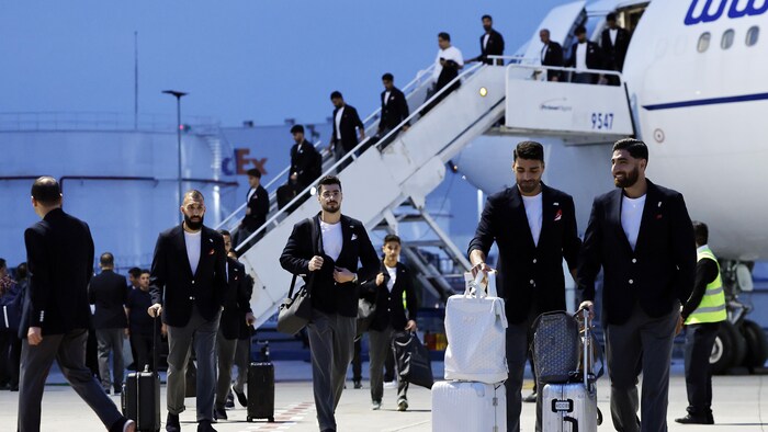 Des hommes en complet descendent d'un avion et marchent sur un tarmac avec des valises. 