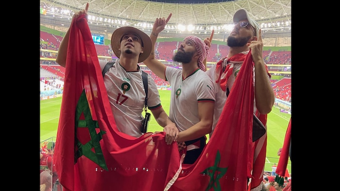 ثلاثة رجال في ملعب يحملون العلم المغربي.